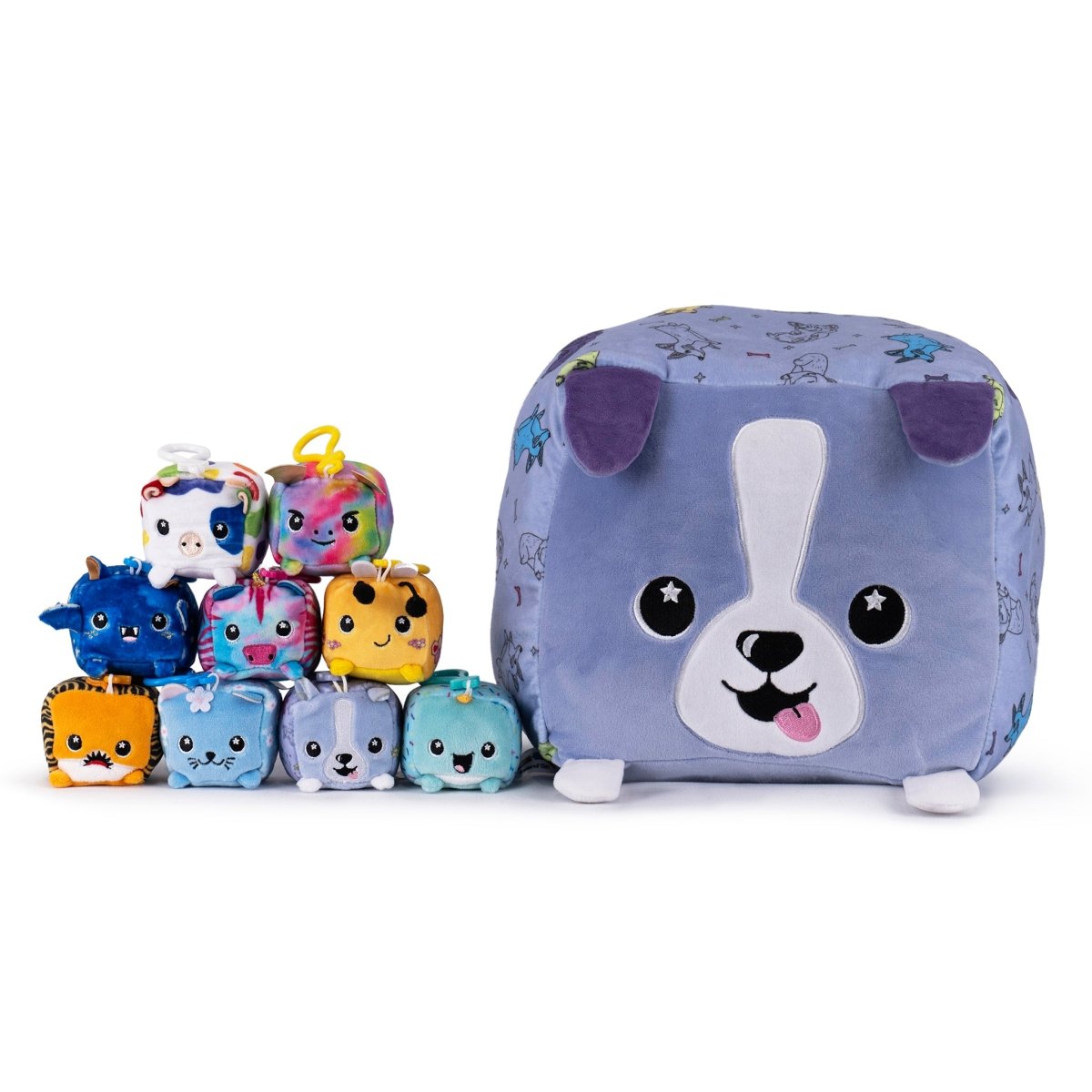 A collection of small, colorful plush toys resembling animals with cartoon-like faces is arranged next to Milly the Cow, a cube-shaped dog plushie from Moosh-Moosh Series 1 with a purple body and playful expression.