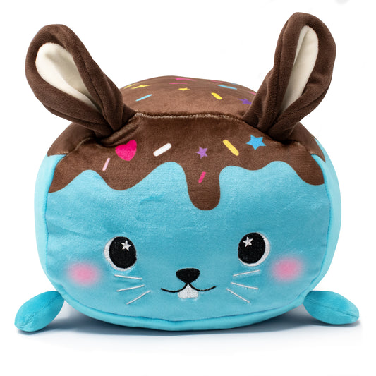 Bitty the Bunny Plushie is a soft, plush toy shaped like a rabbit with a turquoise body, big eyes, a smiling face, brown ears, and a brown topping with colorful sprinkles resembling icing.