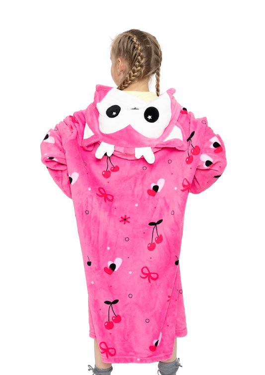 A child with braided hair is seen from behind, wrapped in a bright pink Hooded Blanket - Doe the Deer featuring cherries, hearts, bows, and a hood with a cute cartoon deer face with large eyes and playful ears.