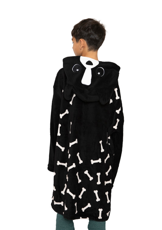 A child faces away, wearing the "Hooded Blanket - Ollie the Corgi," a black kids hooded blanket featuring white bones and an animal face with floppy ears on the hood.