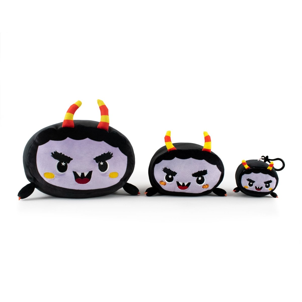 The Moosh-Moosh Spooky Series features Fang the Monster Clip-On, a plush toy shaped like a cartoon bat with a purple face, black body, red and yellow striped horns, and fangs. Available in small, medium, and large sizes.