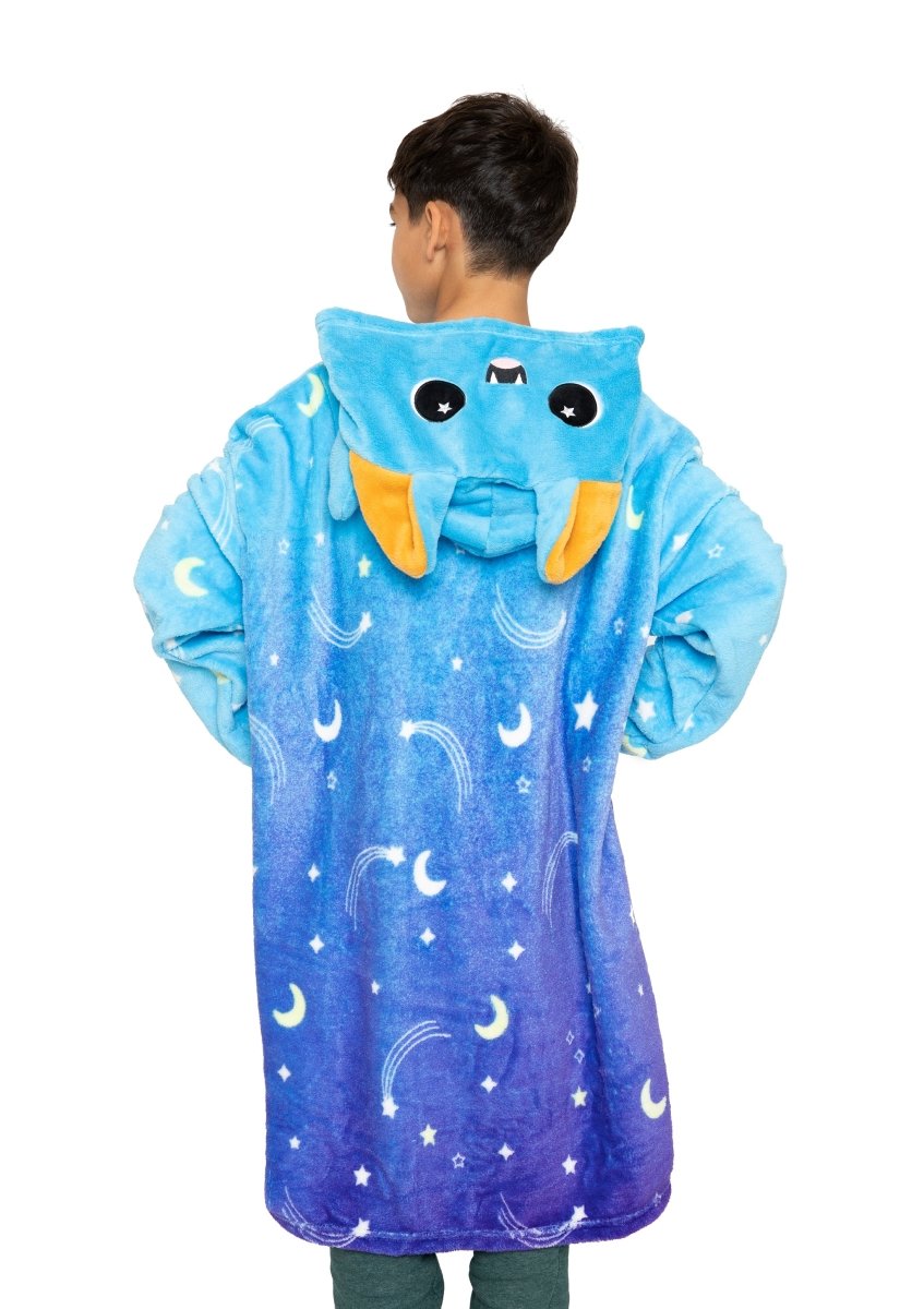 A child is seen from behind wearing the Hiso the Bat Hooded Blanket in blue and purple, featuring a cartoon bat face with moons, stars, shooting stars, bat ears, eyes, teeth, and orange inner ear details.