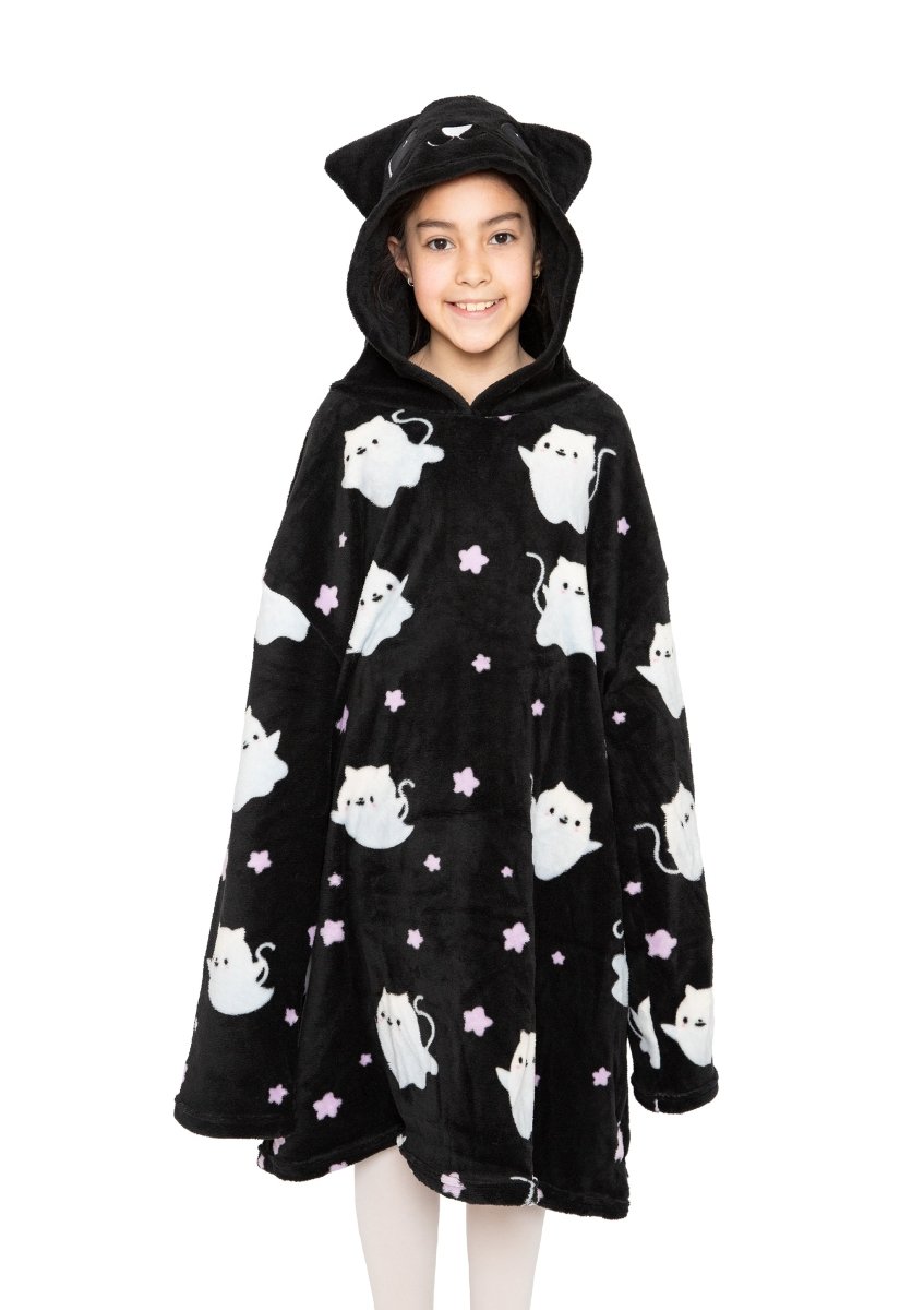 A smiling child wears the Fortune the Cat Hooded Blanket, a black fleece hooded blanket with white cat and pink star prints, plus a hood featuring cat ears and an embroidered face. The background is plain white.