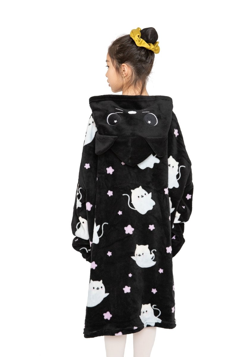 A girl with a yellow scrunchie wears the Fortune the Cat Hooded Blanket, a black fleece robe with white cartoon cats and purple stars. The hood has cat ears and a face. She is turned away, displaying the cozy blanket’s back.