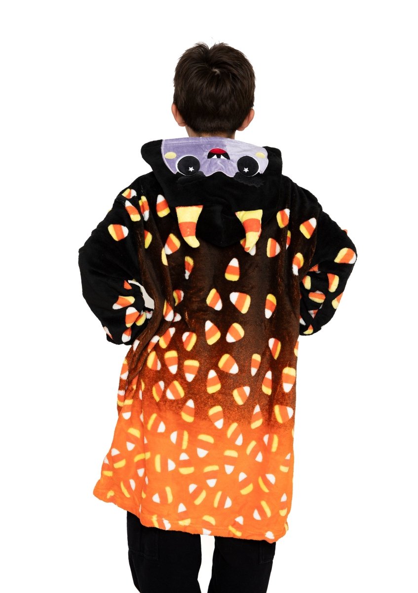 A child faces away, wrapped in the Fang the Monster Hooded Blanket—a cozy black and orange Halloween blanket with a candy corn pattern and an adorable hood featuring round eyes and small ears.