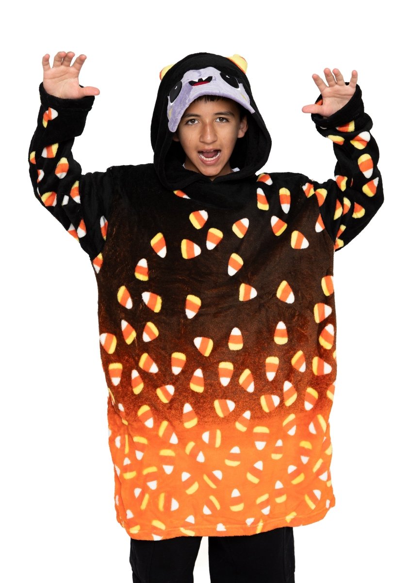 A child wears Fang the Monster Hooded Blanket—an oversized black and orange Halloween blanket with candy corn patterns, playful animal-like ears, and a cute face—raising their arms with a grin, perfect for spooky Halloween fun.