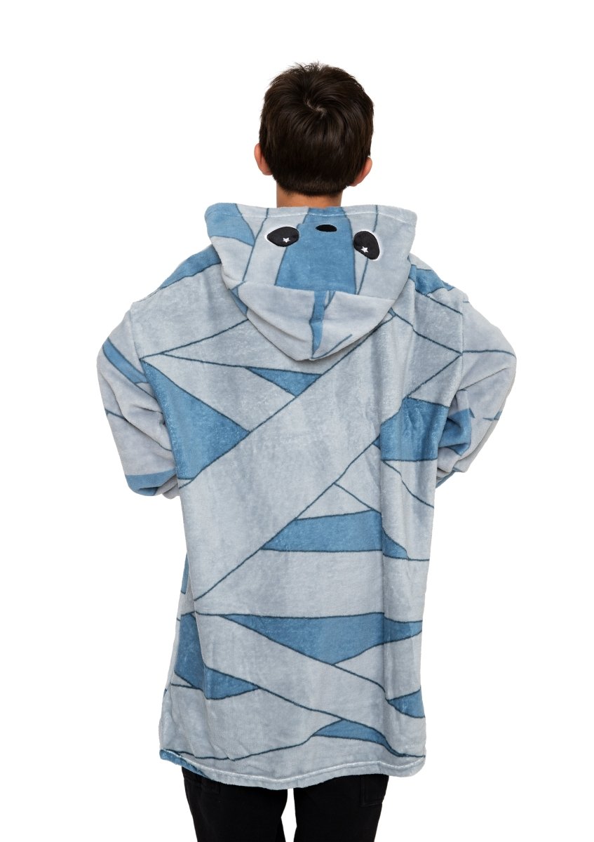 A person faces away, wearing the Nile the Mummy Hooded Blanket—a cozy blue kids fleece blanket with wide cartoon eyes and bandage patterns, perfect for Halloween.