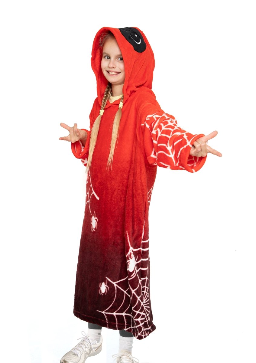 A smiling young girl wears the Muffet the Spider Hooded Blanket, covered in white spider webs and cartoon spiders, standing with arms outstretched and making a playful hand gesture.