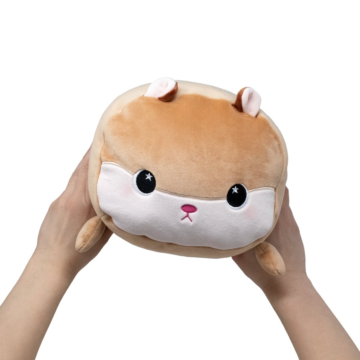 A pair of hands holds Hammy the Hamster, a round brown and white plush toy with large black eyes, small ears, and a cute pink nose, against a plain white background.
