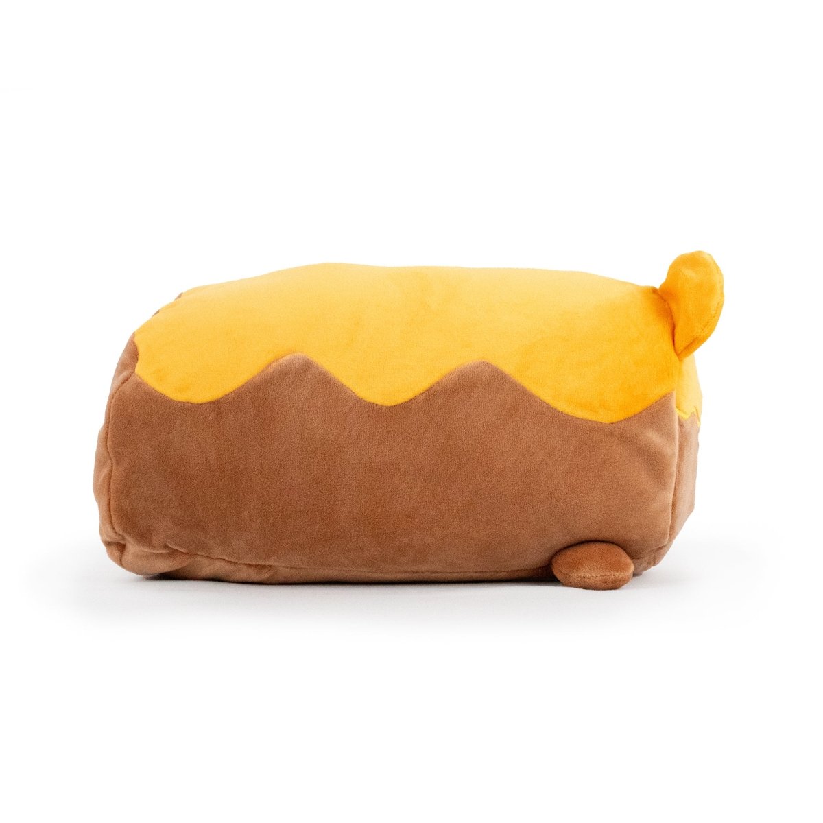 Meet the Moosh-Moosh family's charming new member—Honey the Bear Plushie. Shaped like a loaf of bread, it showcases a brown base and yellow crust-like top, complete with small plush feet and a subtle tail-like detail, embodying the whimsical essence of these beloved toys.
