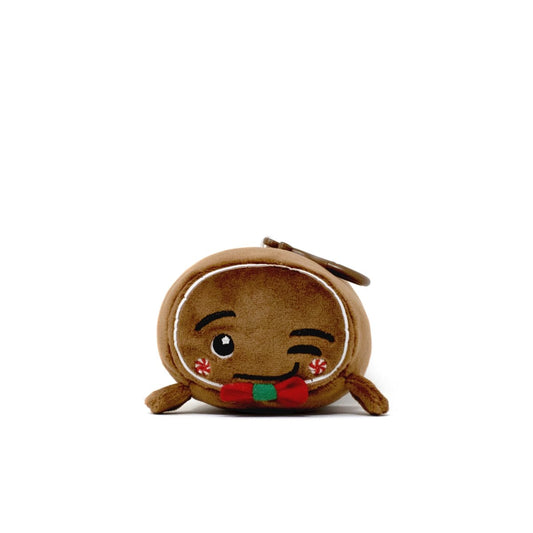 The Gingersnaps Clip-On is a small, round holiday plushie resembling a winking gingerbread cookie, featuring embroidered details, red cheeks, a red and green bow tie, and a plush keychain clip on top.