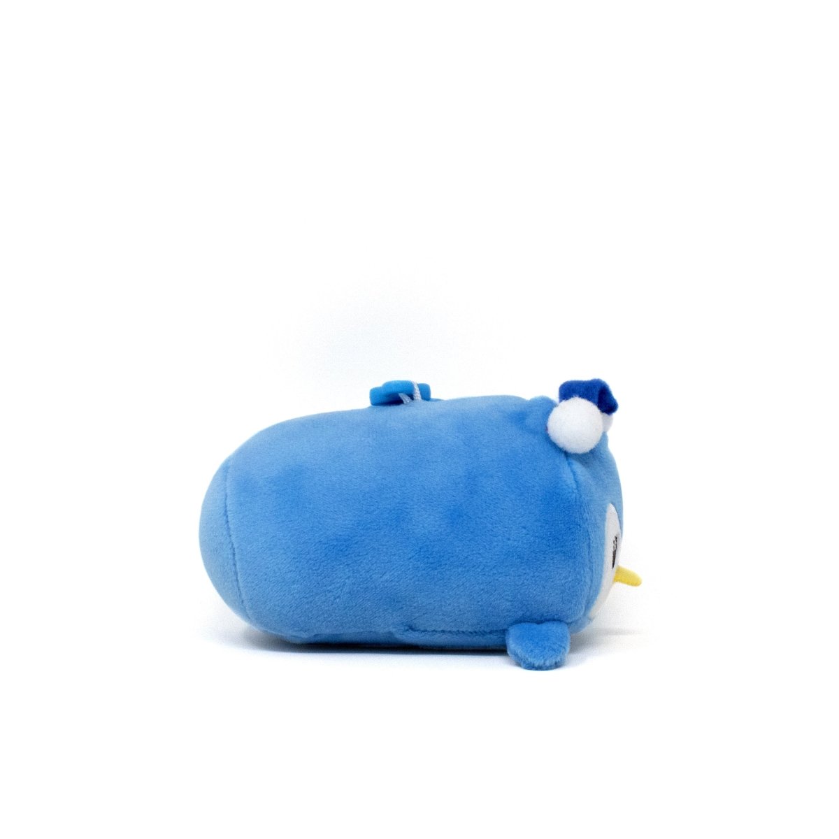 Peckington the Penguin Clip-On, a cute plushie shaped like a blue penguin, lies on its side showcasing soft flippers and a small yellow beak. A white pom-pom adorns its head, enhancing its charm against the plain white background.