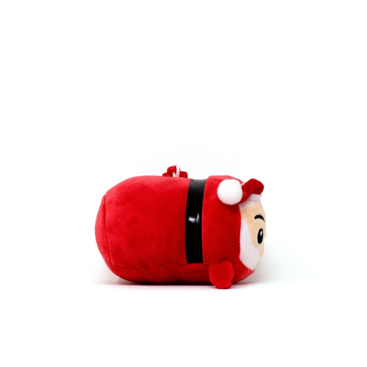 The Santa Clip-On is a small, round red Christmas plushie dressed as Santa Claus, featuring a white beard, red hat with pom-pom, black belt, and embroidered face, shown lying on its side against a plain white background.