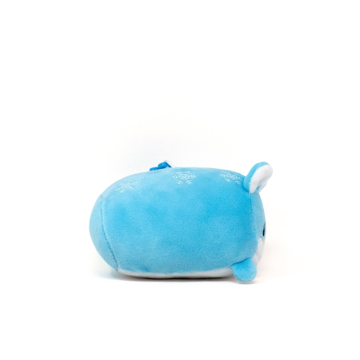 Yuki the Snow Fox Clip-On is a small, round blue stuffed animal resembling a seal, with white snowflake patterns on its soft back. It features tiny flippers, a white underside, and an adorable face with black eyes on a white background.