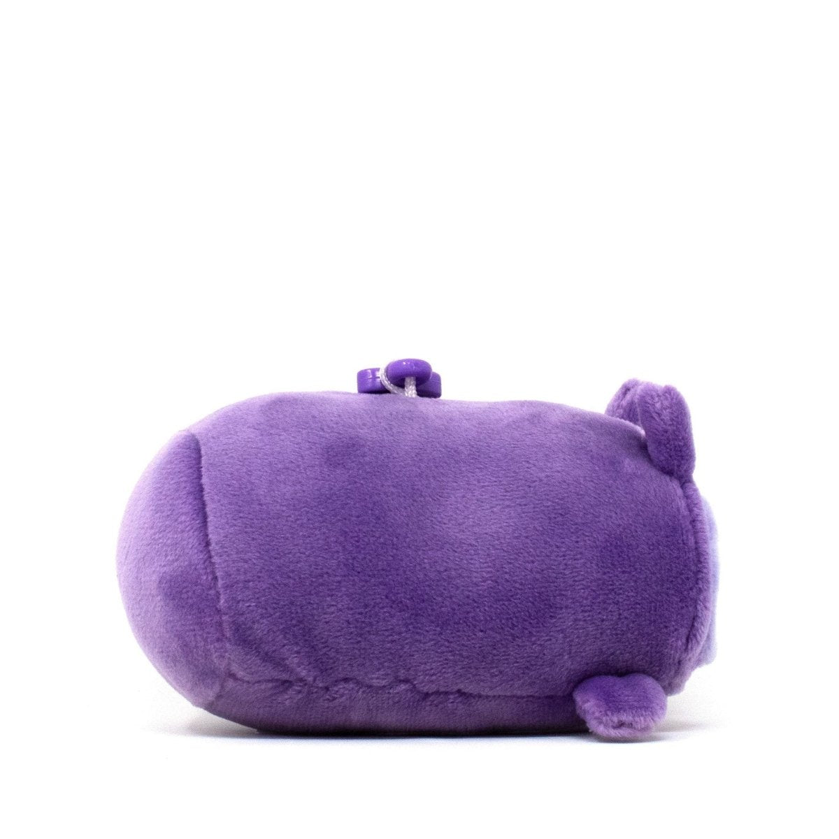 Archie the Owl Clip-On is a cute plushie shaped like a purple capsule with small ears and a tiny tail. Its soft, velvety fabric invites cuddles as it rests on its side against a plain white background.