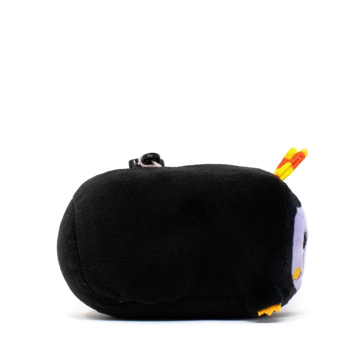 Fang the Monster Clip-On, a small, round black plush from the Moosh-Moosh Spooky Series with a purple face, yellow beak, and tiny yellow feet, lies on its side against a white background.