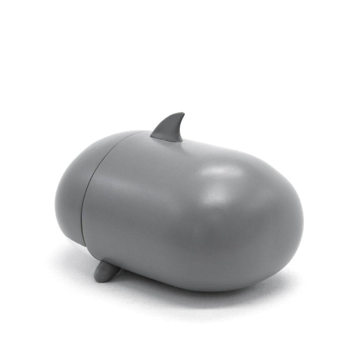 The Crush the Shark Vinyl Collectible Figurine is a small, smooth, gray object with a rounded body, two tiny fins on the sides, and a dorsal fin on top. This adorable shark-shaped figure is an excellent addition to your Moosh-Moosh collection and is set against a plain white background.