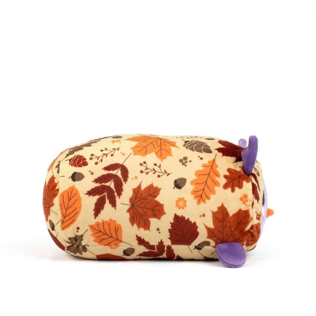 The Archie Spooky Slumber Plushie is a cylindrical plush toy with an autumn leaf pattern in orange, brown, and red. Made from ultra-soft materials, it has small purple ears and horns on a light background—ideal for cozy cuddles.