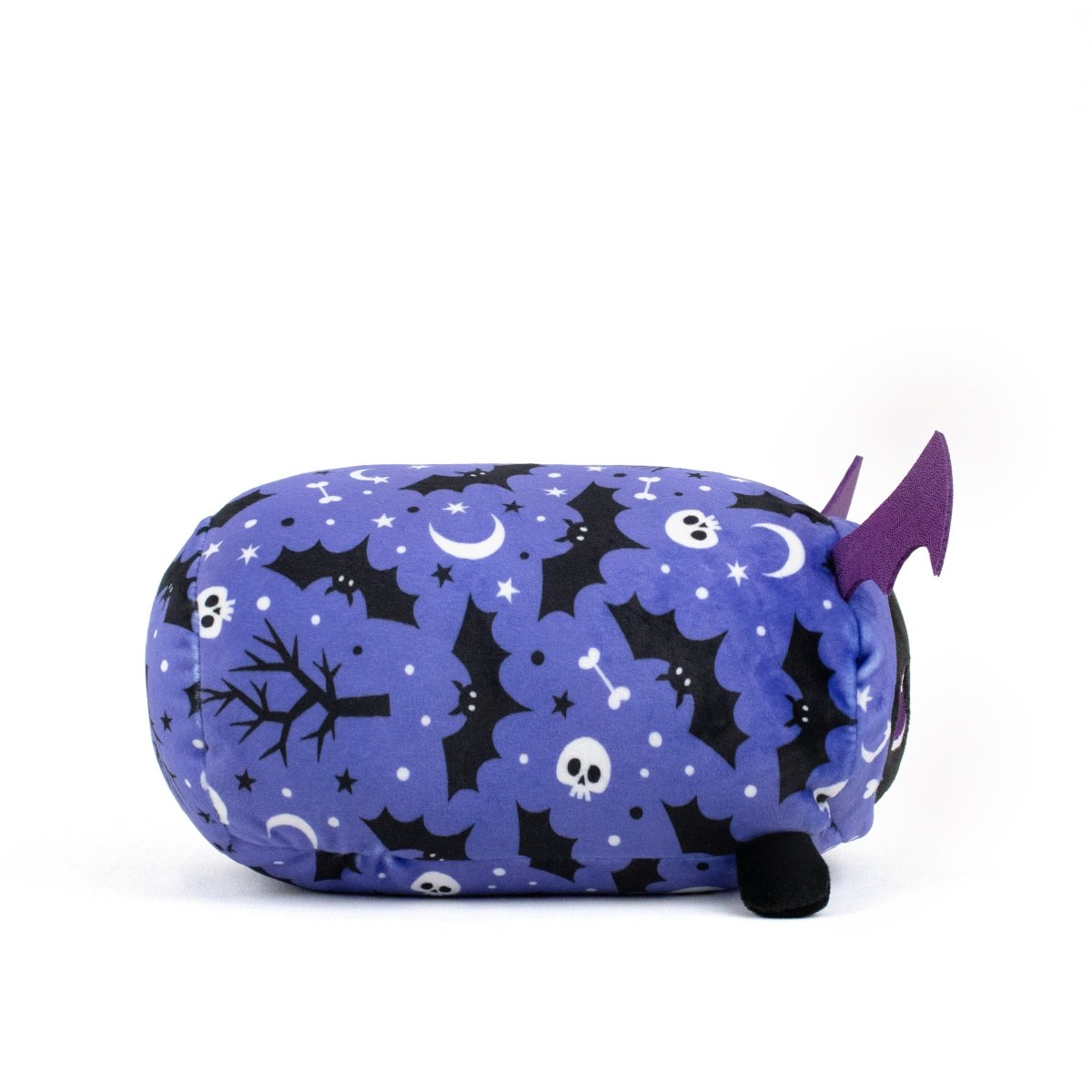 The Cassie Spooky Slumber Plushie is a cylindrical plush toy made from ultra-soft purple fabric featuring bats, skulls, moons, and trees, with small black legs and purple bat wings on one side.