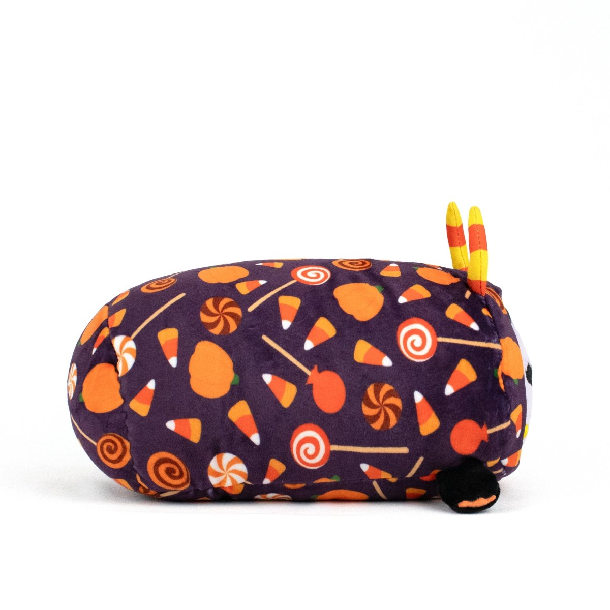 The Fang Spooky Slumber Plushie is a long oval plush toy made with ultra-soft purple fabric featuring orange pumpkins, candy corn, and lollipops. It has small yellow-orange horns, tiny black feet, and is machine washable for easy care.