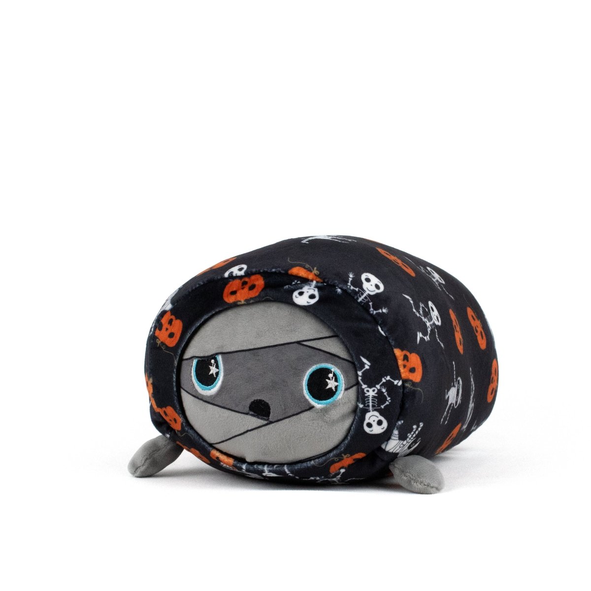 The Nile Spooky Slumber Plushie is a mummy-shaped toy made from ultra-soft materials, wrapped in black fabric with orange pumpkins and white skeletons. It has large blue eyes, a gray face, and a cute, round look.