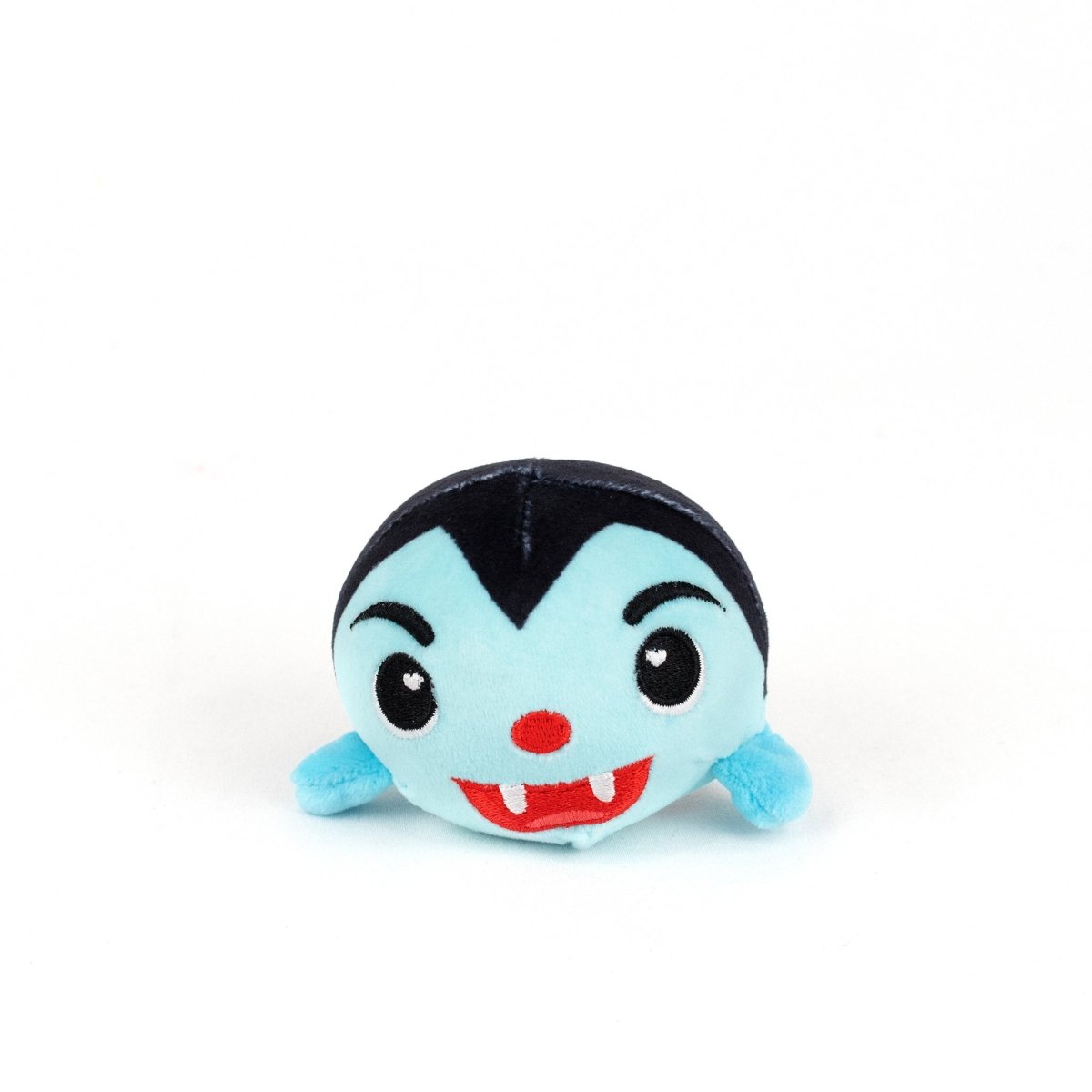 The Vlad Spooky Plushy Skwishy is a small, round plush toy with a blue face, black hair, red nose, fangs, tiny blue arms, and a cheerful expression—resembling a cute cartoon vampire.