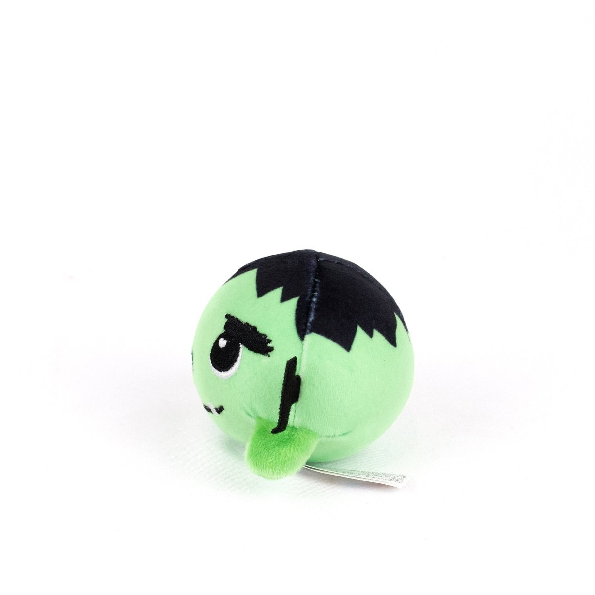 The Frankie Spooky Plushy Skwishy is a round, green plush toy with black hair and stitched details inspired by Frankenstein’s monster, shown at a slight angle on a white background.