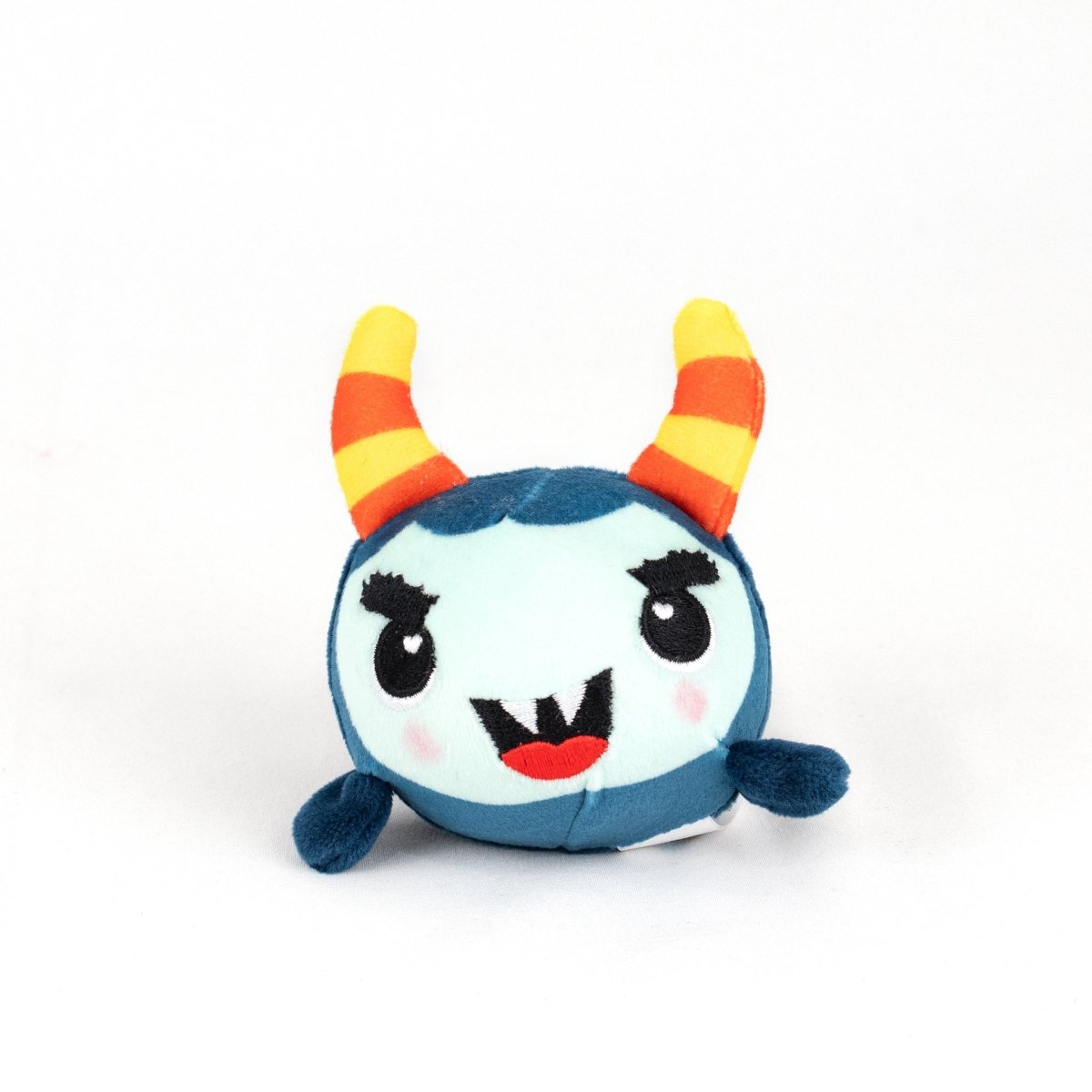 The Spike Spooky Plushy Skwishy is a round, blue plush toy with a light blue face, orange and yellow striped horns, black eyebrows, small fangs, blushing cheeks, and tiny flipper-like arms set against a white background.