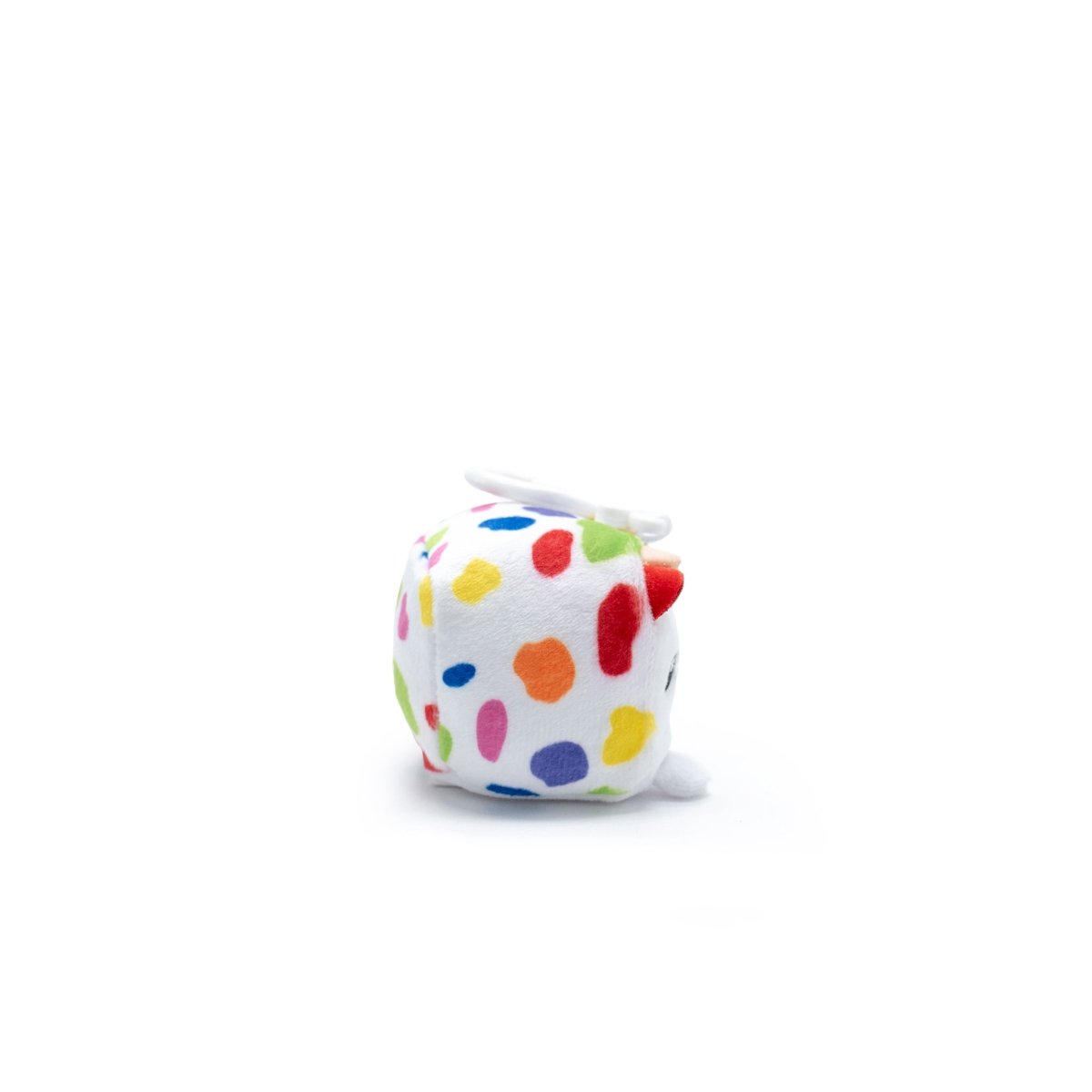 A small, white plushie with colorful polka dots lies on its side against a plain white background. It's Milly the Cow Square Plush Clip-On from Moosh-Moosh Series 1, featuring a red nose and black eyes.