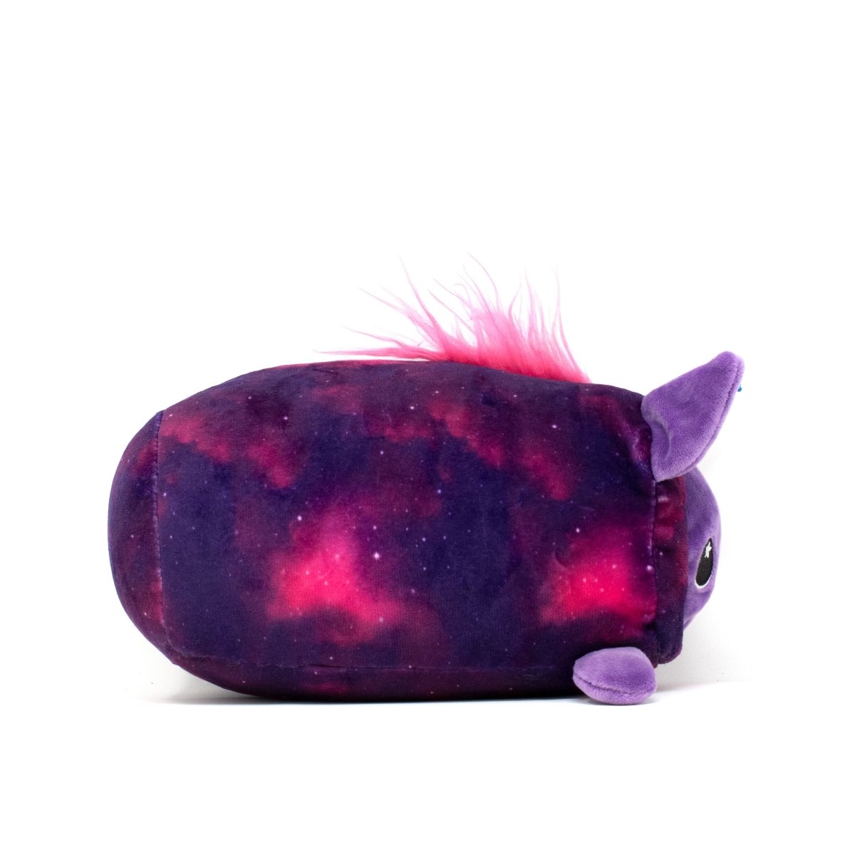 The Twinkle Slumber Plushie is an oval-shaped toy with a cosmic pink and purple pattern reminiscent of a unicorn's dream, showcasing small purple ears and a tuft of pink hair on top, elegantly positioned on its side against a white background.