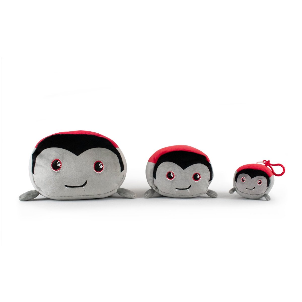 Bram the Vampire Plushie from the Moosh-Moosh Spooky Series features a gray face, black markings, red back, small legs, and a smile. The smallest has a red keychain clip. A cute Halloween stuffed animal on a white background.