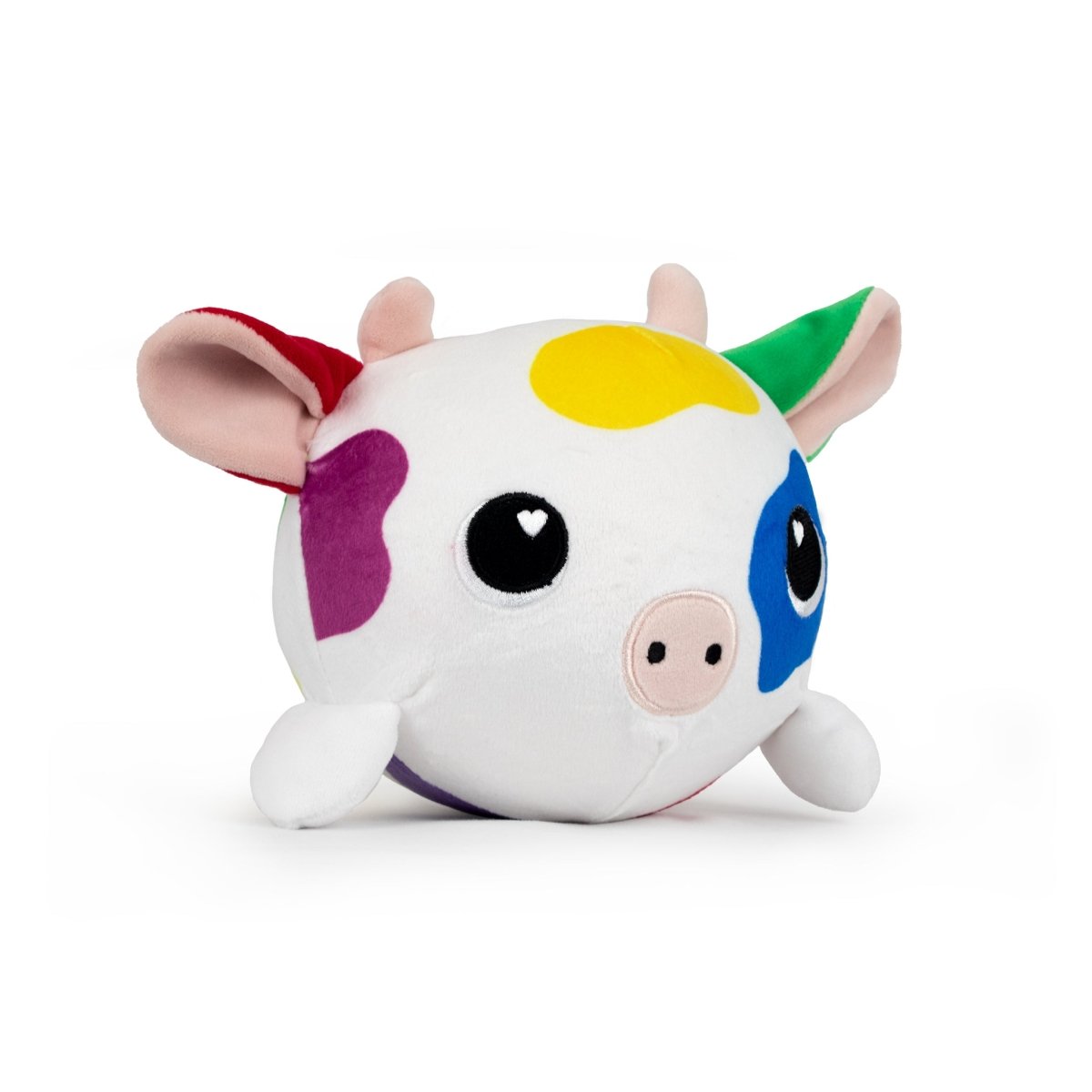 The Jumbo Plushy Skwishy Clara is a round cow-shaped toy with big black eyes and a small snout, featuring multicolored patches in yellow, blue, purple, and red. It has pink inside its ears and horns that are red and green.
