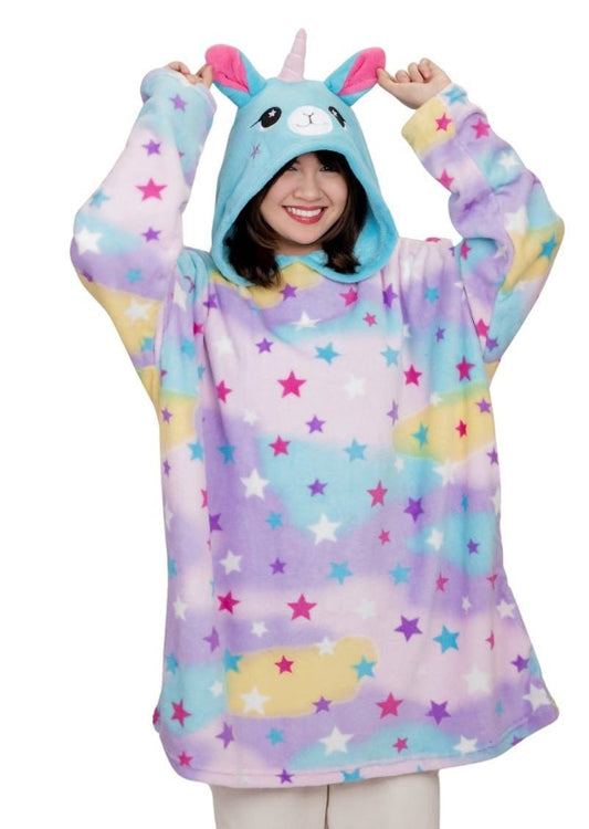 A person smiles wearing the Llamacorn Hooded Blanket—an oversized pastel hoodie with colorful stars, clouds, a unicorn face, horn, and ears. They playfully hold up the hood’s ears, resembling a whimsical character blanket.