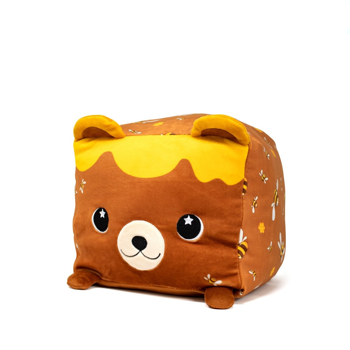 Introducing Mel Bee the Bear Plushie—a soft, cube-shaped pillow. It has small ears, big eyes, and a cute smile. Honey and bee patterns adorn its sides like a honeycomb with tops resembling dripping honey. This charming plushie is mostly brown and yellow.