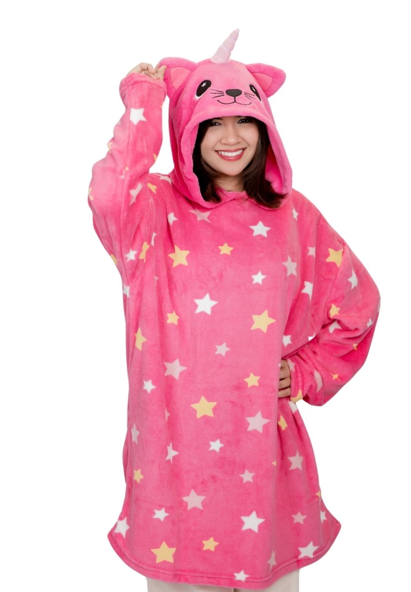 A person smiles wrapped in a soft, oversized Caticorn Hooded Blanket. This pink, star-patterned fleece features an animal face on the hood complete with a whimsical horn and ears, as they playfully hold one side.