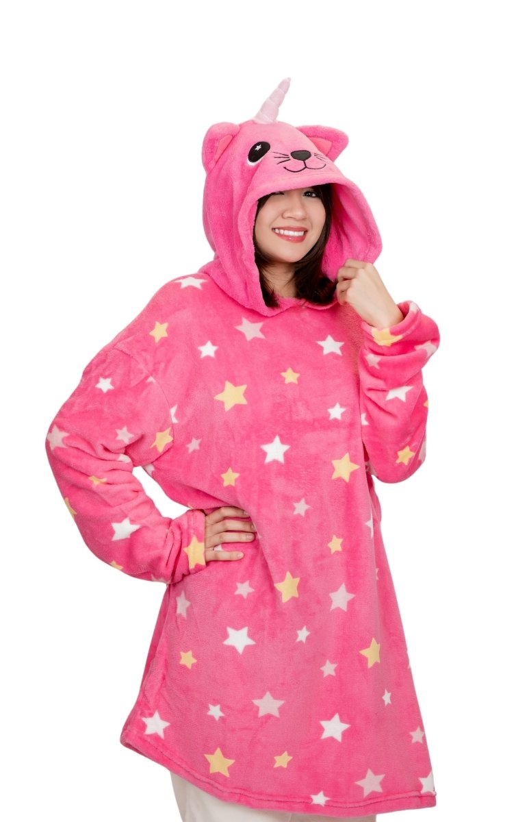 A person smiles in a pink oversized Caticorn Hooded Blanket, featuring a unicorn and cat design. The whimsical fleece hoodie has stars and a horn on the hood, blending seamlessly against a white background.