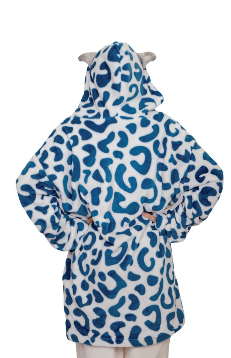 Model stands hands-on-hips, back to camera, wearing Snowie the Leopard Hooded Blanket—a cozy, holiday-inspired design with blue spots and playful animal ears—set against a plain white background.