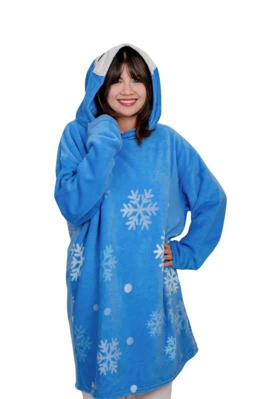 A smiling person wears the Peckington the Penguin Hooded Blanket, a cozy blue fleece with white snowflakes and dots—perfect as a holiday gift.
