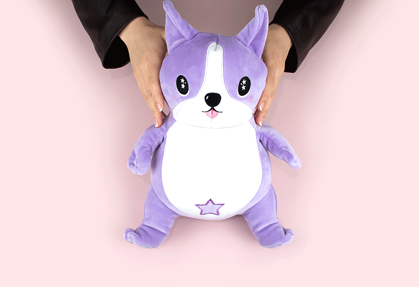 A person’s hands holding a cute, purple plush toy shaped like a dog with big eyes, a white belly, and a star on its lower abdomen, against a pink background.