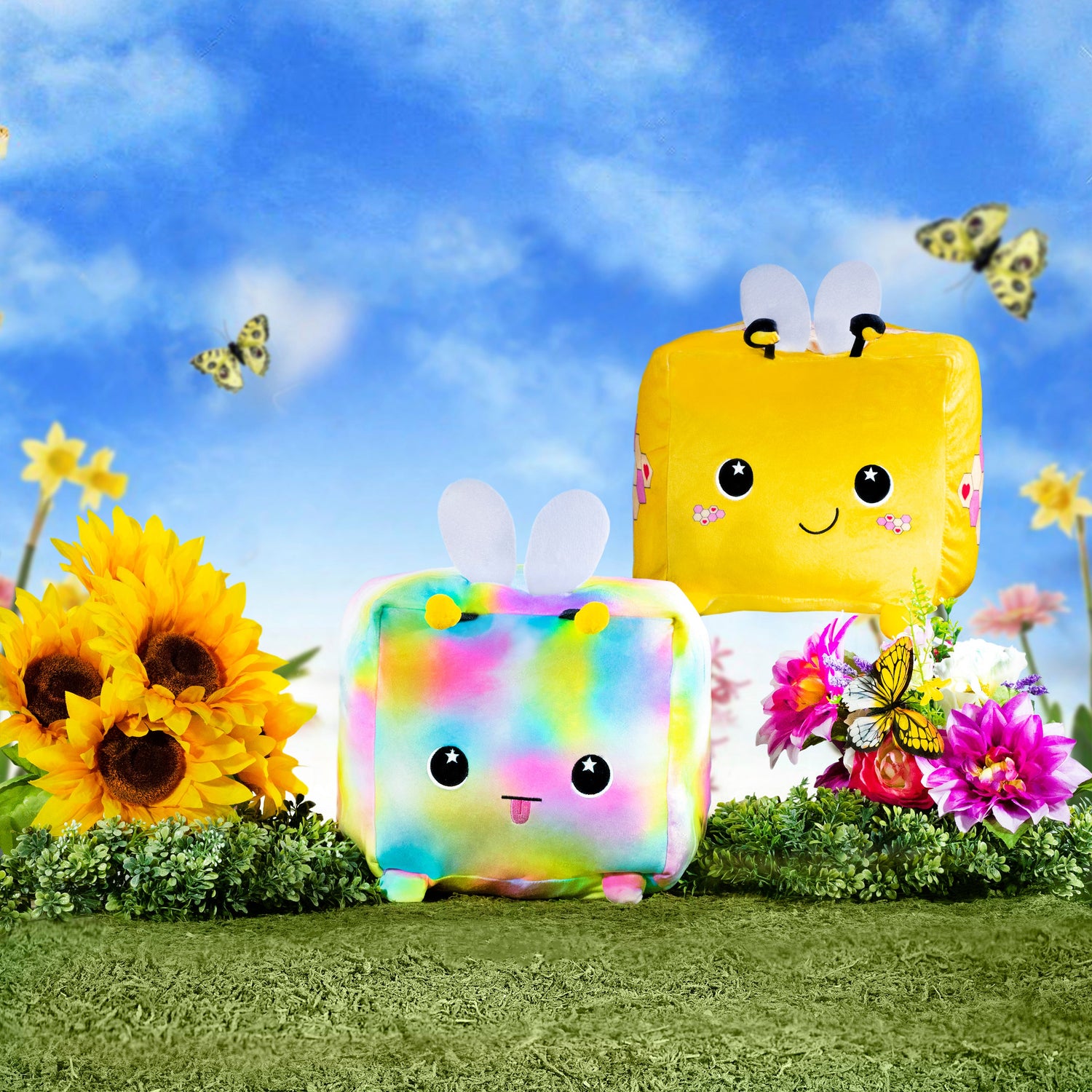 Two Moosh-Moosh Squared Plush, Hex and Flora, relax on the grass surrounded by flowers.