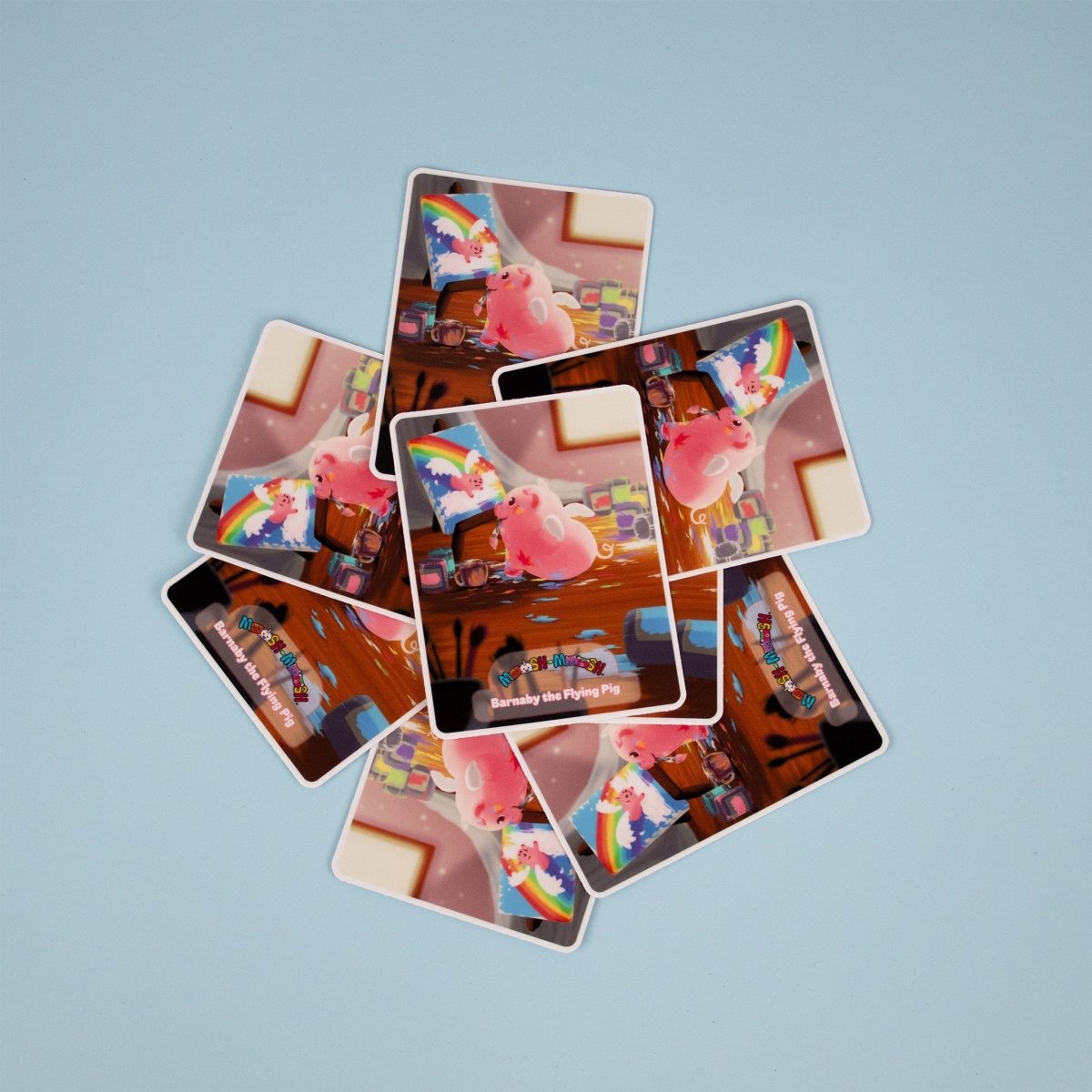 A circle of Moosh-Moosh 3" x 4" Vinyl Stickers is arranged on a light blue surface, each featuring an illustrated pink pig with a rainbow cape flying above suitcases and a wooden floor, with some stickers overlapping.