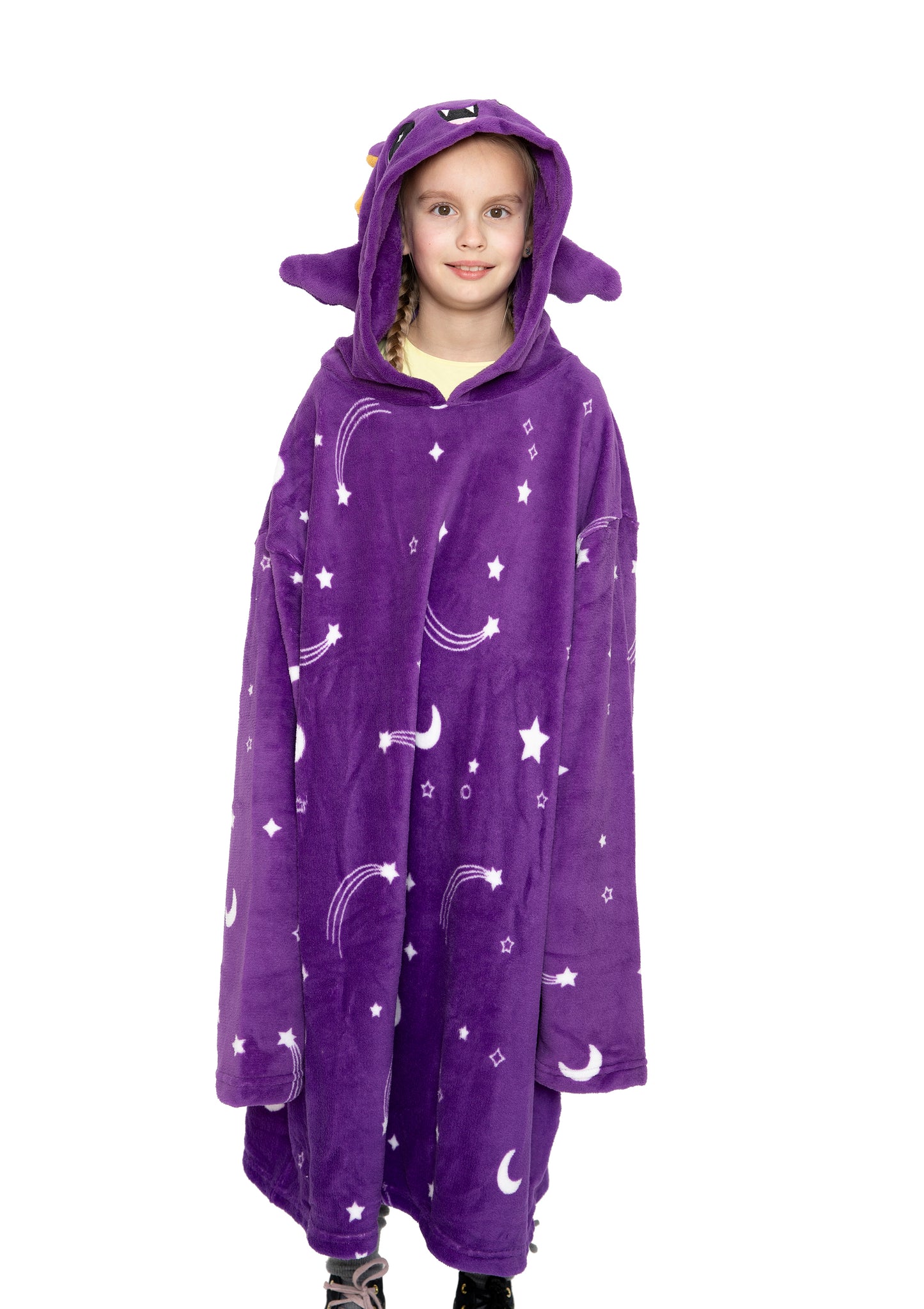 A young girl wears the Hooded Blanket - Oswald the Bat, a large purple blanket with white stars, moons, rainbows, and an animal-eared hood featuring Oswald's face. She stands against a plain white background.