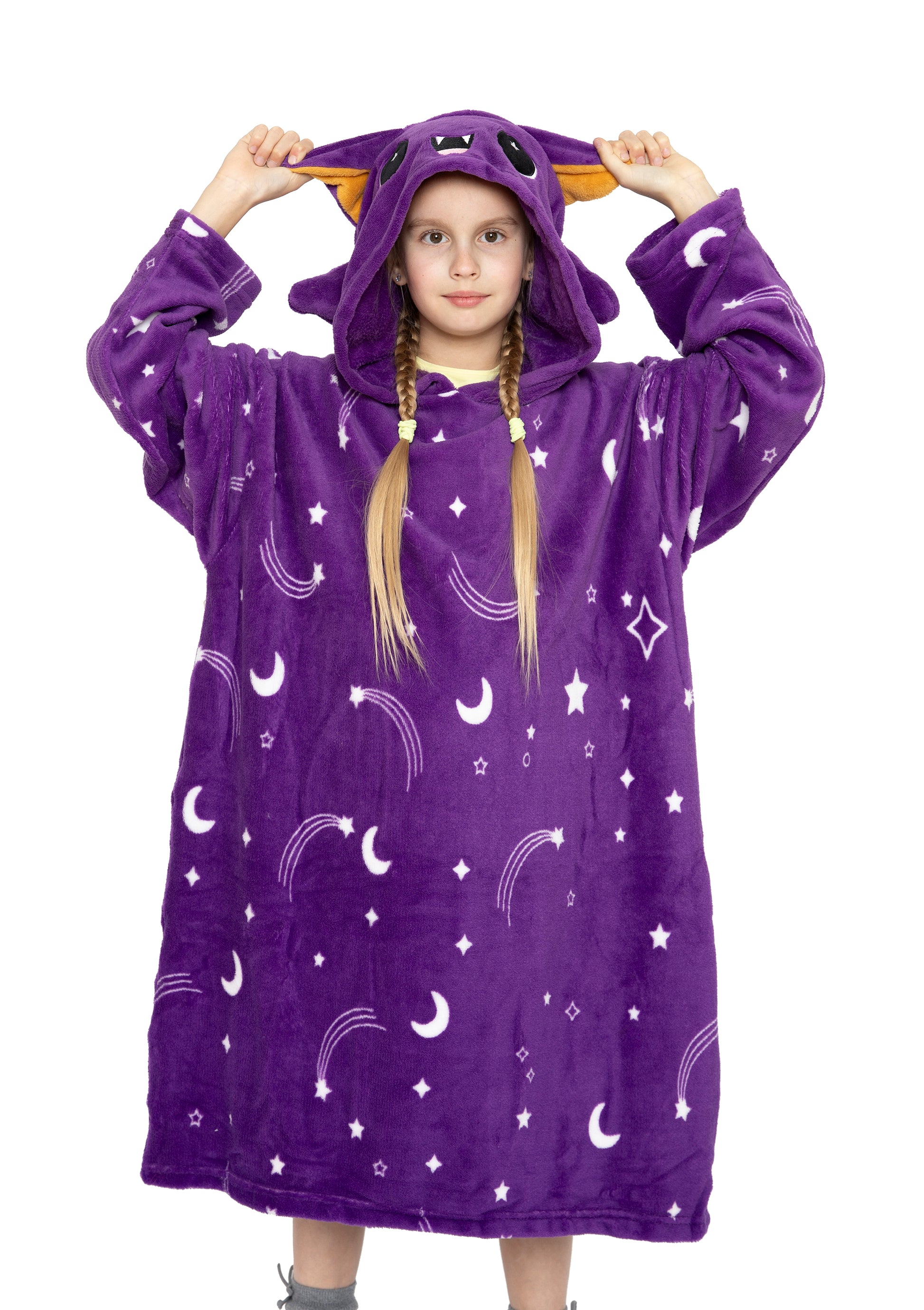A young girl wears the Hooded Blanket - Oswald the Bat, featuring a purple design with moon and star patterns, cat-like ears, and a cute face. She faces forward, showing her long blond hair styled in braids.
