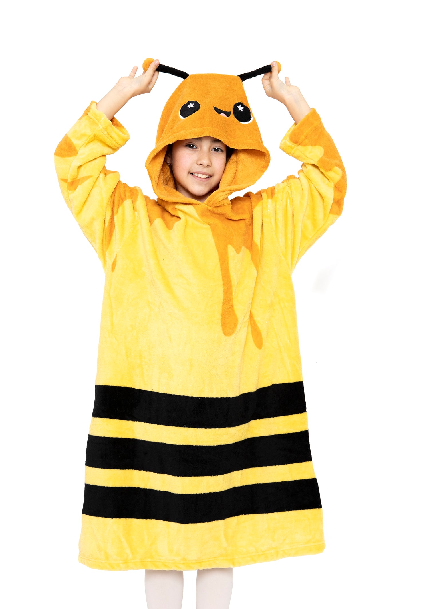 A child smiles while wearing the Hooded Blanket - Vee the Bee, a yellow and black kids fleece blanket with antennae and a cute face on the hood, holding the antennae against a white background.