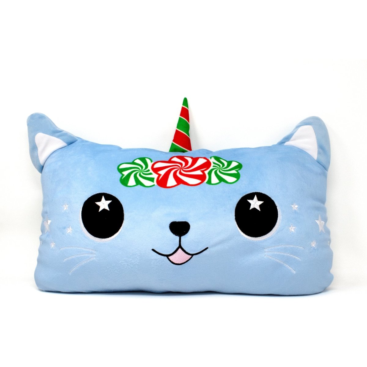 The Kira the Caticorn Pillow is a blue, rectangular plush featuring a cute cartoon cat face with starry eyes, a small pink tongue, white whiskers, and sports a red-green striped horn along with a wreath of red and white flowers around its head.