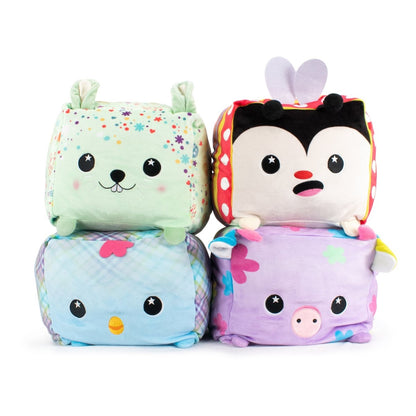 Four delightful Easter stuffed animals are stacked in a 2x2 arrangement, offering sensory softness: a green bunny with floral patterns is top left, beside Avril the Ladybug Plushie, while the bottom row features a blue bird and a purple pig adorned with abstract designs.