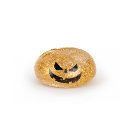 A small, round, gold glittery jelly toy called Bubblegum’s Favorite Toy - Spooky Mystery Dumpling, featuring a black jack-o’-lantern face design, sits on a white background.