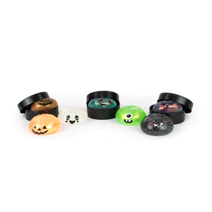 Seven Bubblegum’s Favorite Toy - Spooky Mystery Dumpling squishy figures, featuring colorful round designs with cute cartoon faces such as a pumpkin and a cyclops, are displayed with two black open containers on a white background.