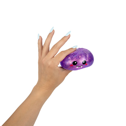A hand with light blue nails squeezes Bubblegum’s Favorite Toy - Spooky Mystery Dumpling, a purple, glittery squishy toy featuring a cute, smiling face with pink cheeks, against a white background.