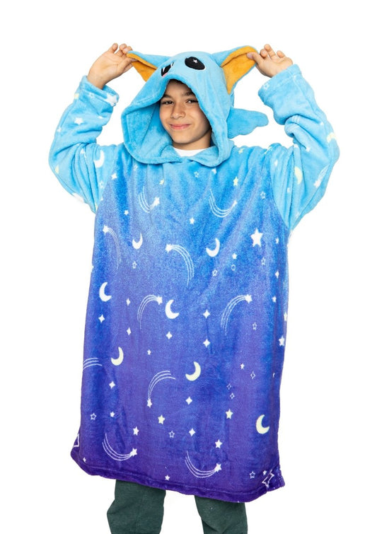 A child smiles while wearing the Hiso the Bat Hooded Blanket, a cozy blue and purple kids blanket with a bat hood featuring large ears and embroidered eyes, decorated with moon and star patterns for a cute fantasy look.